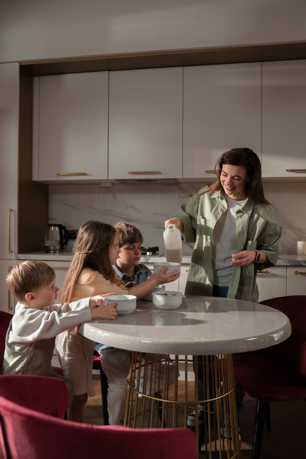 A mother in a kitchen pouring milk for three children sitting at a breakfast table